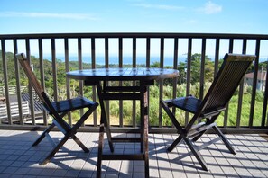 A balcony with a table and two chairs, overlooking a scenic view of the ocean and greenery. - Ryu-a (Nakijin)