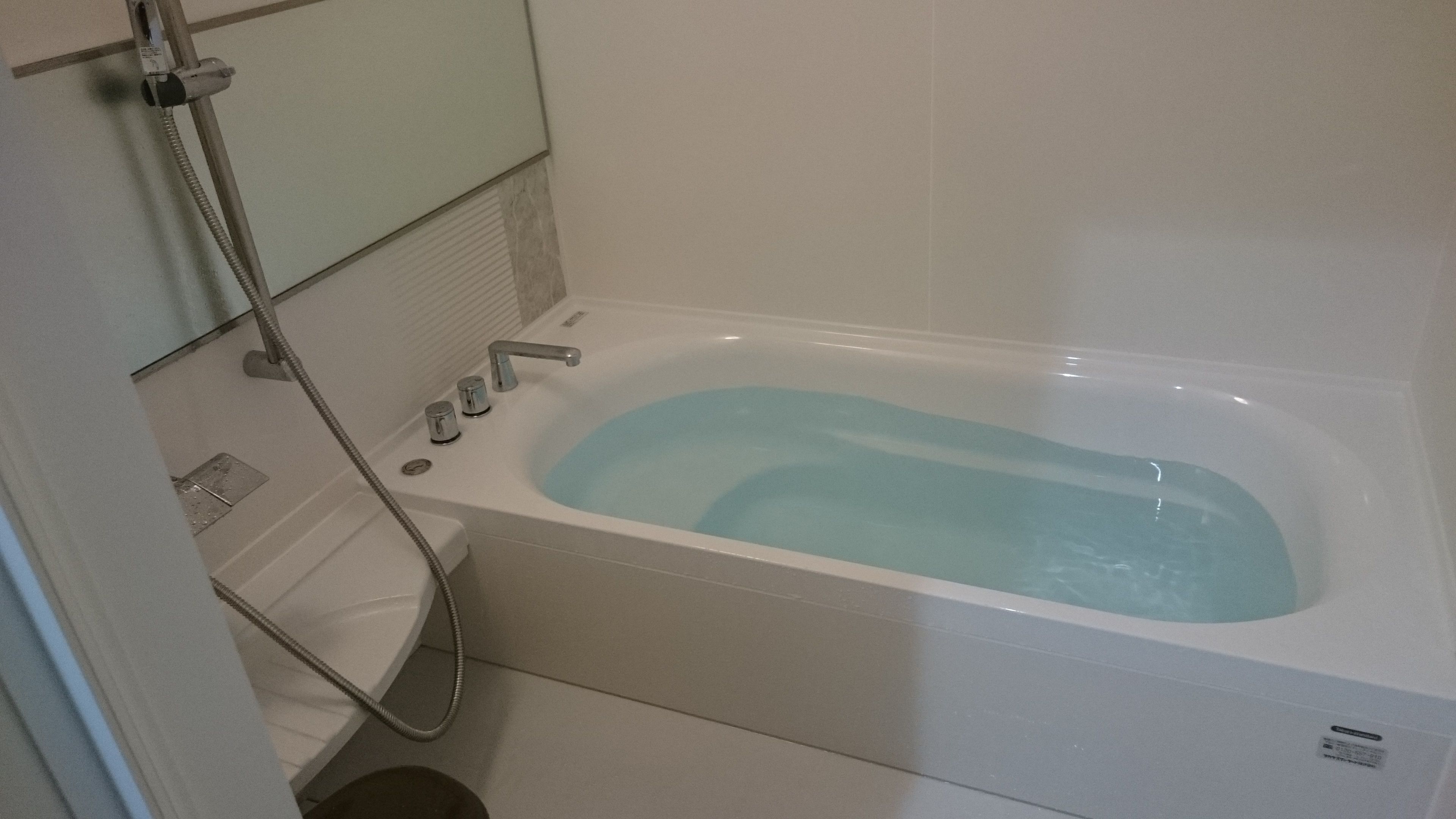 Una bañera blanca estándar con ducha de mano, panel de control y un pequeño ventanuco para ventilación.