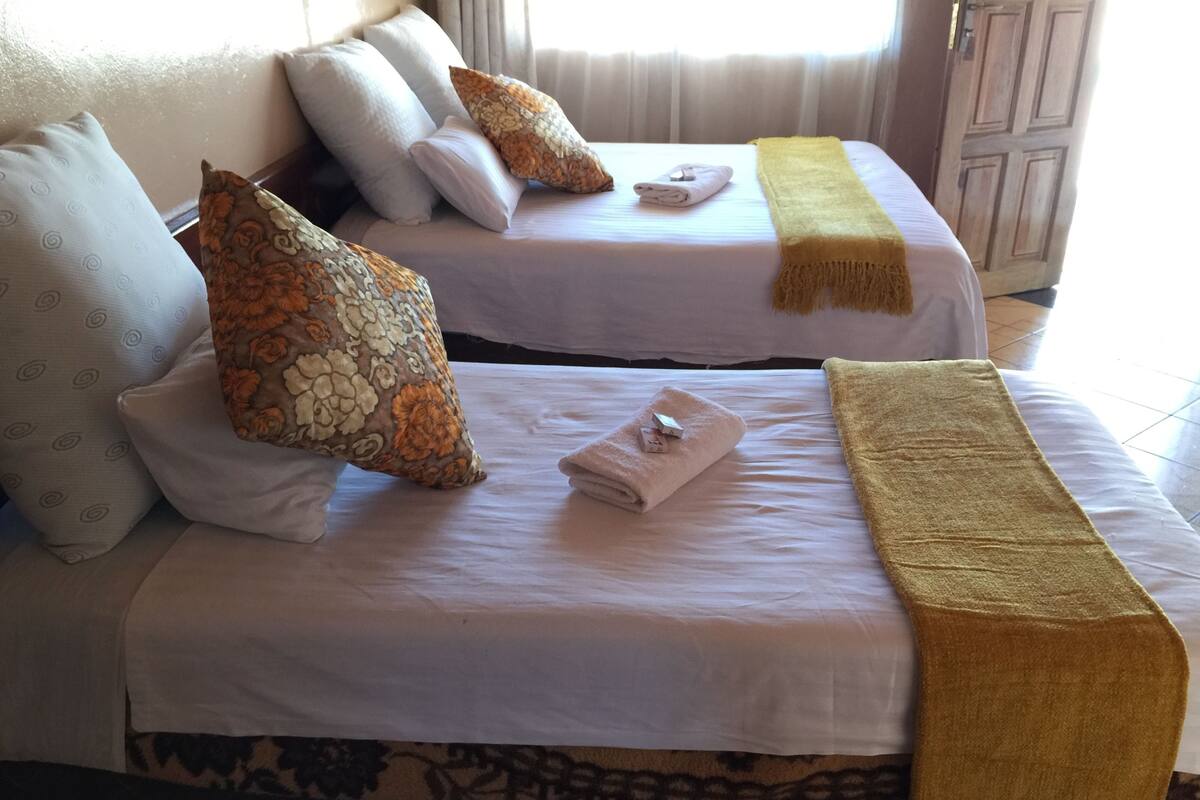 Two twin beds with white linens, floral-patterned pillows, and a yellow throw blanket.