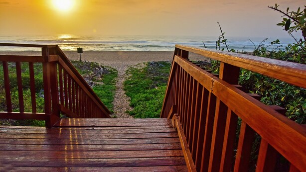 A wooden staircase leading to a beach with a sunset in the background.