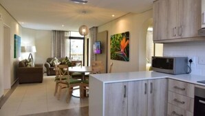 A modern kitchen with wooden cabinets, a dining area with a table and chairs, and a living room with a sofa and a TV.