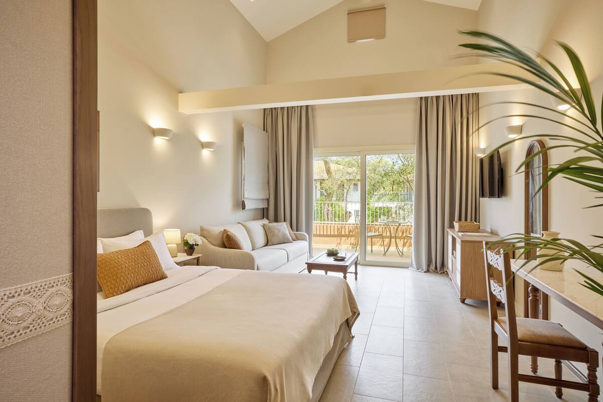 A spacious bedroom with a large bed, a sofa, a desk, and a balcony with curtains.