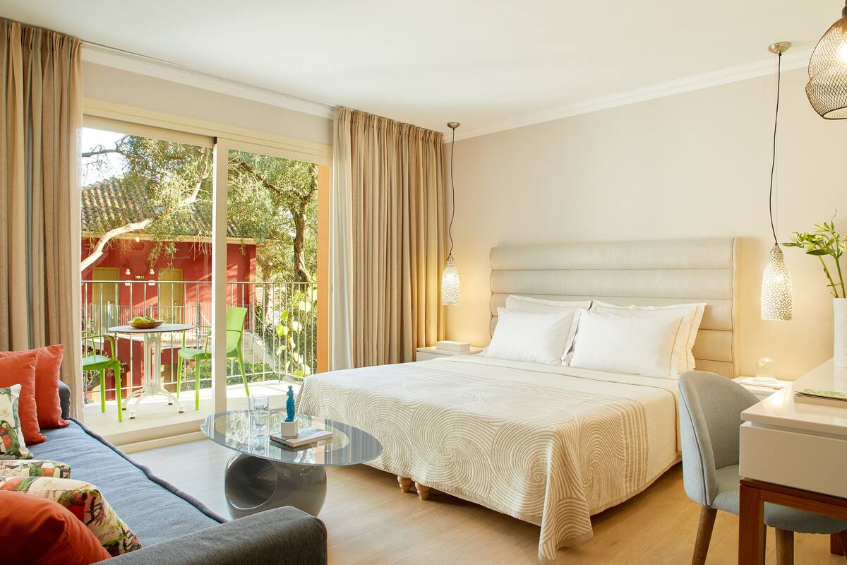 A hotel room with a large bed, a glass coffee table, a desk, and a view of the outdoors.