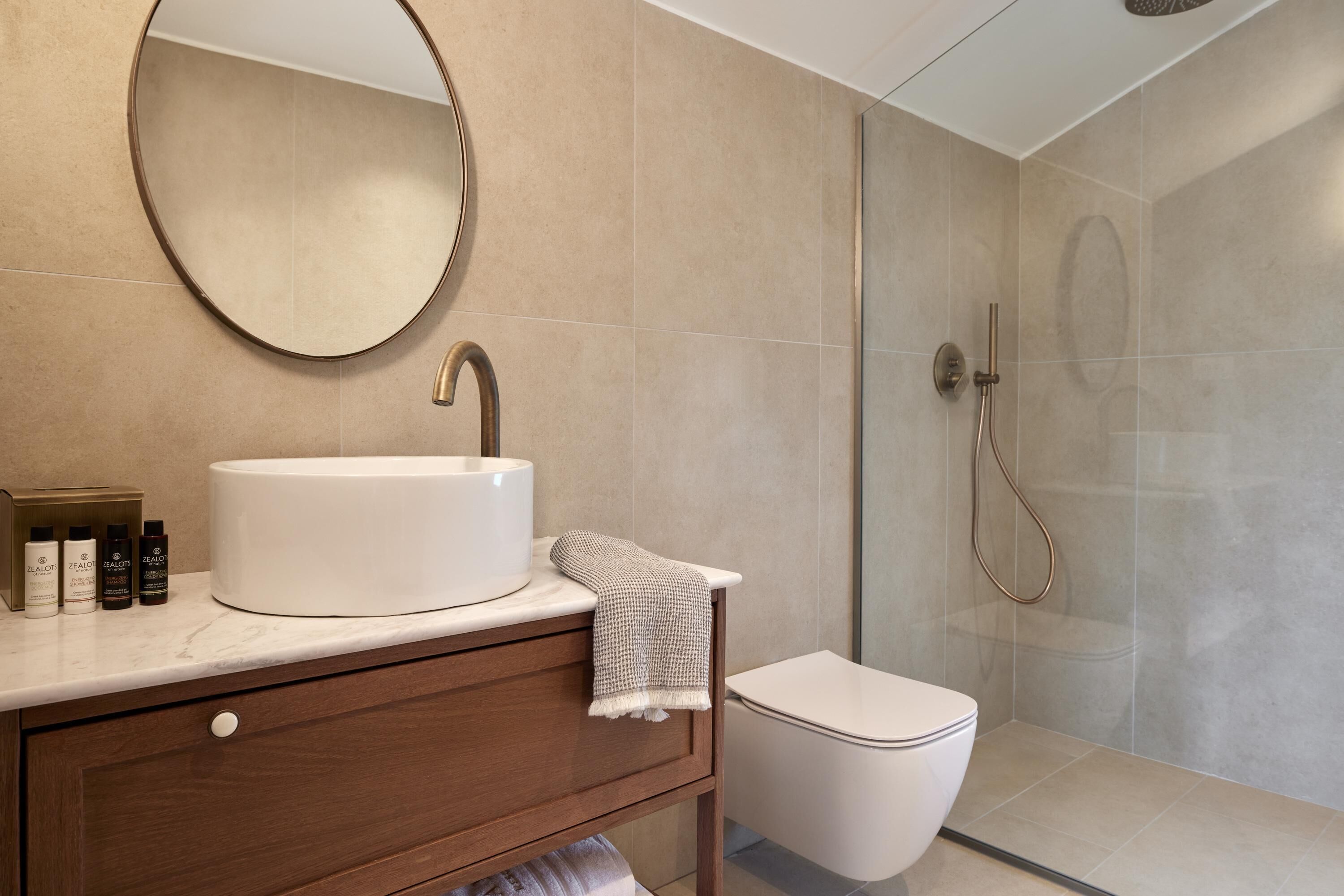 A bathroom with a round mirror, a sink, a towel, and a shower.