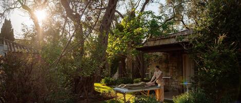 A person meditating on a bench in a lush garden with a stone building in the background.