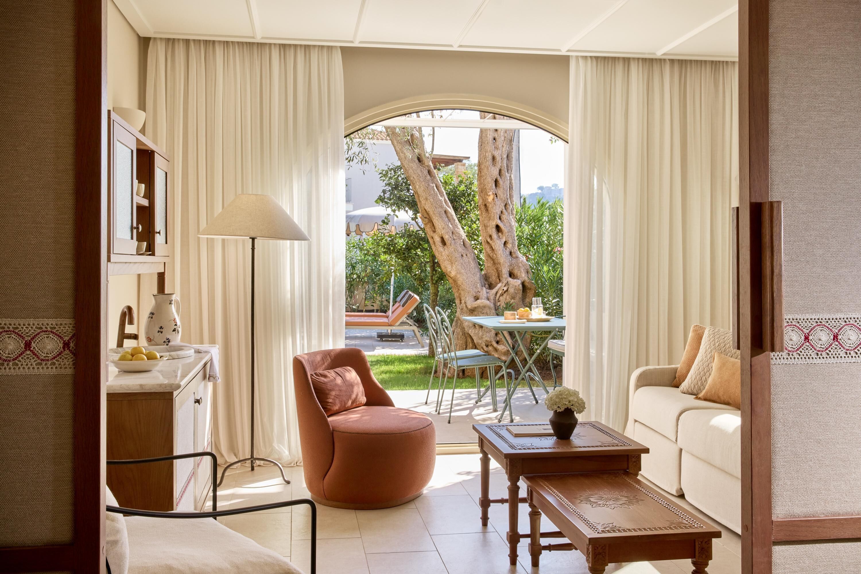 A modern living room with a round orange chair, a wooden coffee table, and a beige sofa. There is a dining table with chairs outside the window.