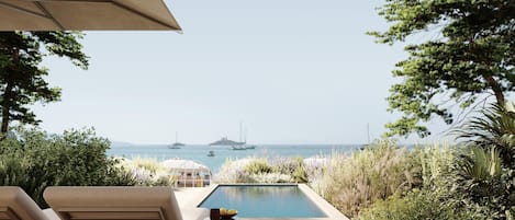 A pool area with lounge chairs and an umbrella, overlooking the sea with boats in the distance.