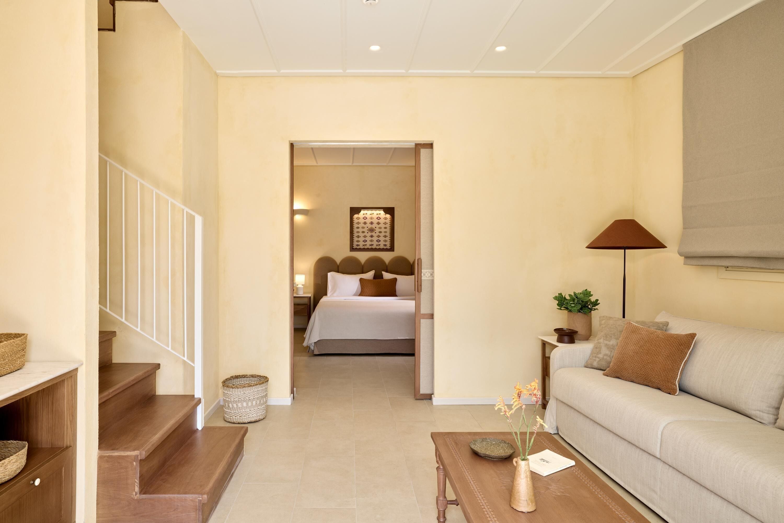 A modern hotel room with a staircase, a bed with a headboard, a sofa, a coffee table, and a lamp.