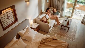 Quarto de hotel com cama, sofá, uma mesinha e vista para a varanda.