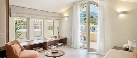 A modern living room with a sofa, a chair, a small table, and a balcony with a view of the mountains.