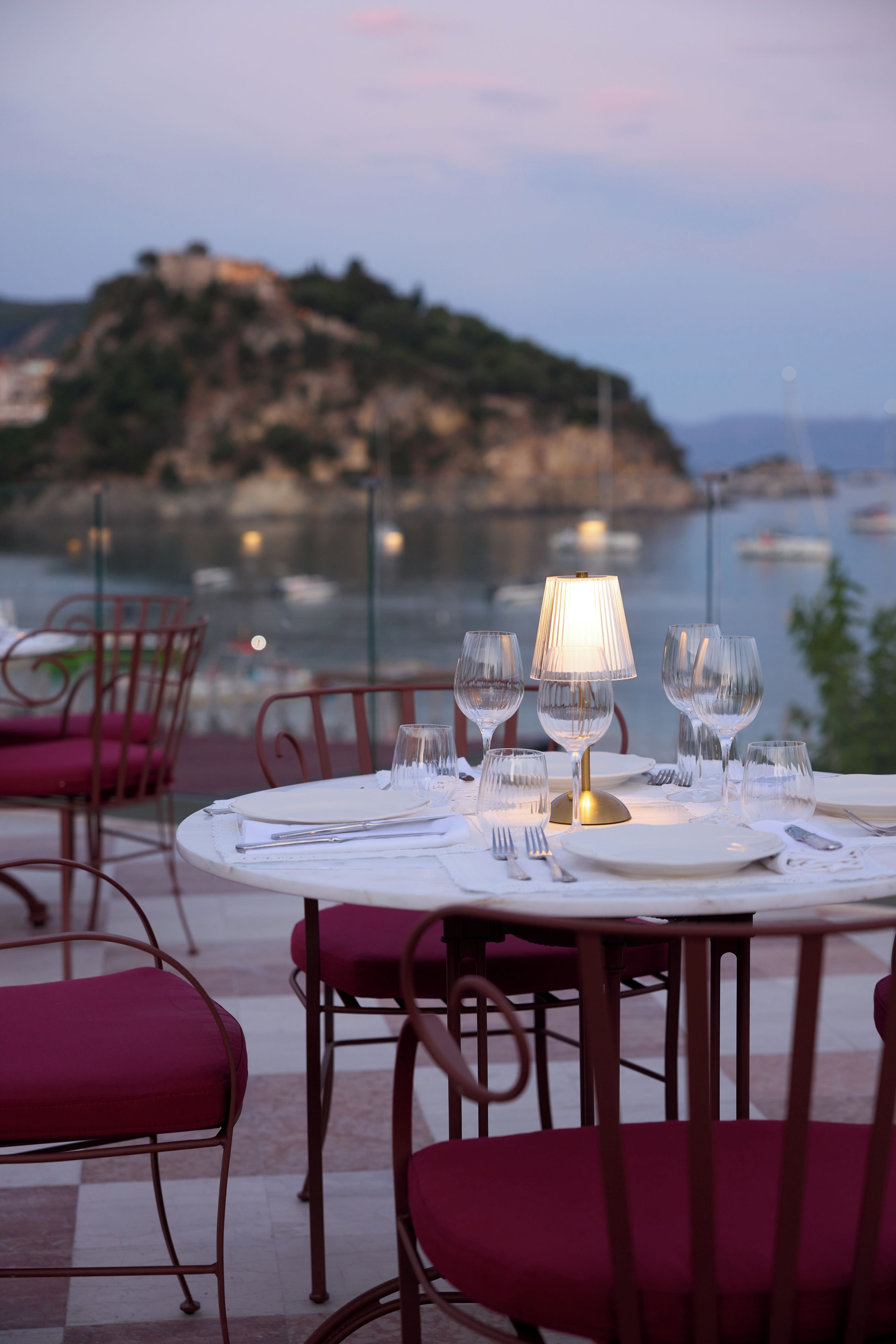 A table set for dining with a view of the sea and a hilly landscape in the background.