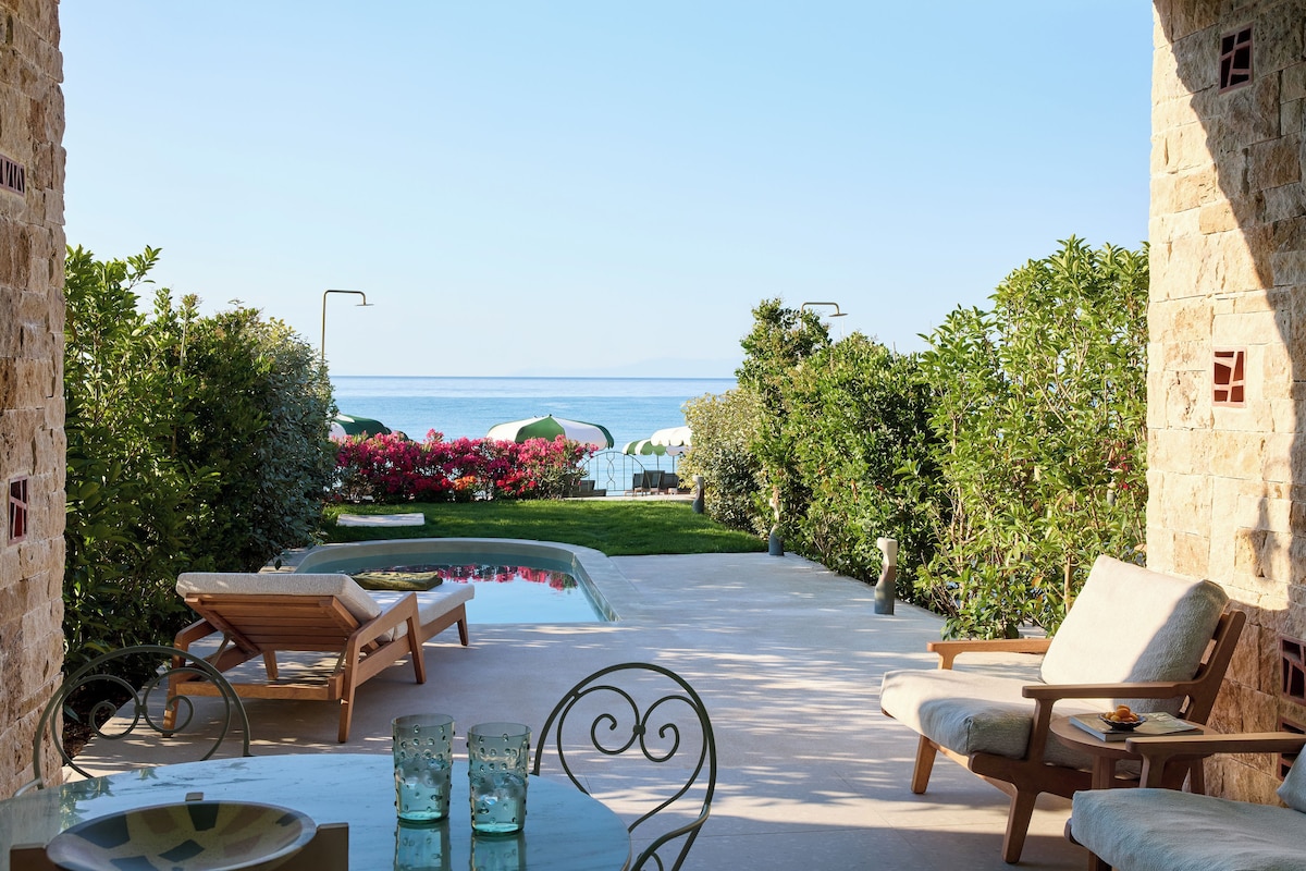 A poolside area with lounge chairs, a small table, and a view of the sea.