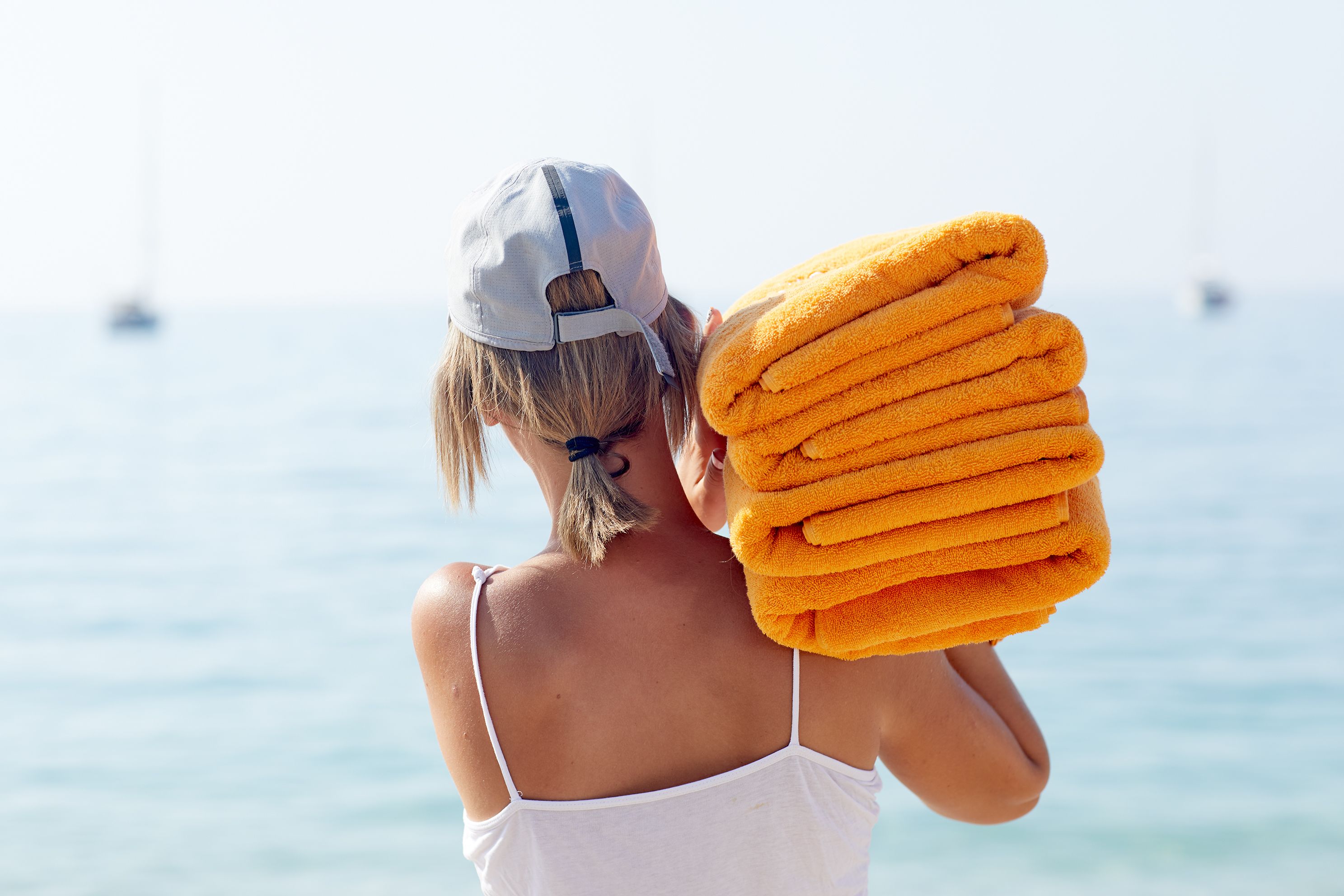 A person holding a stack of towels by the seaside.