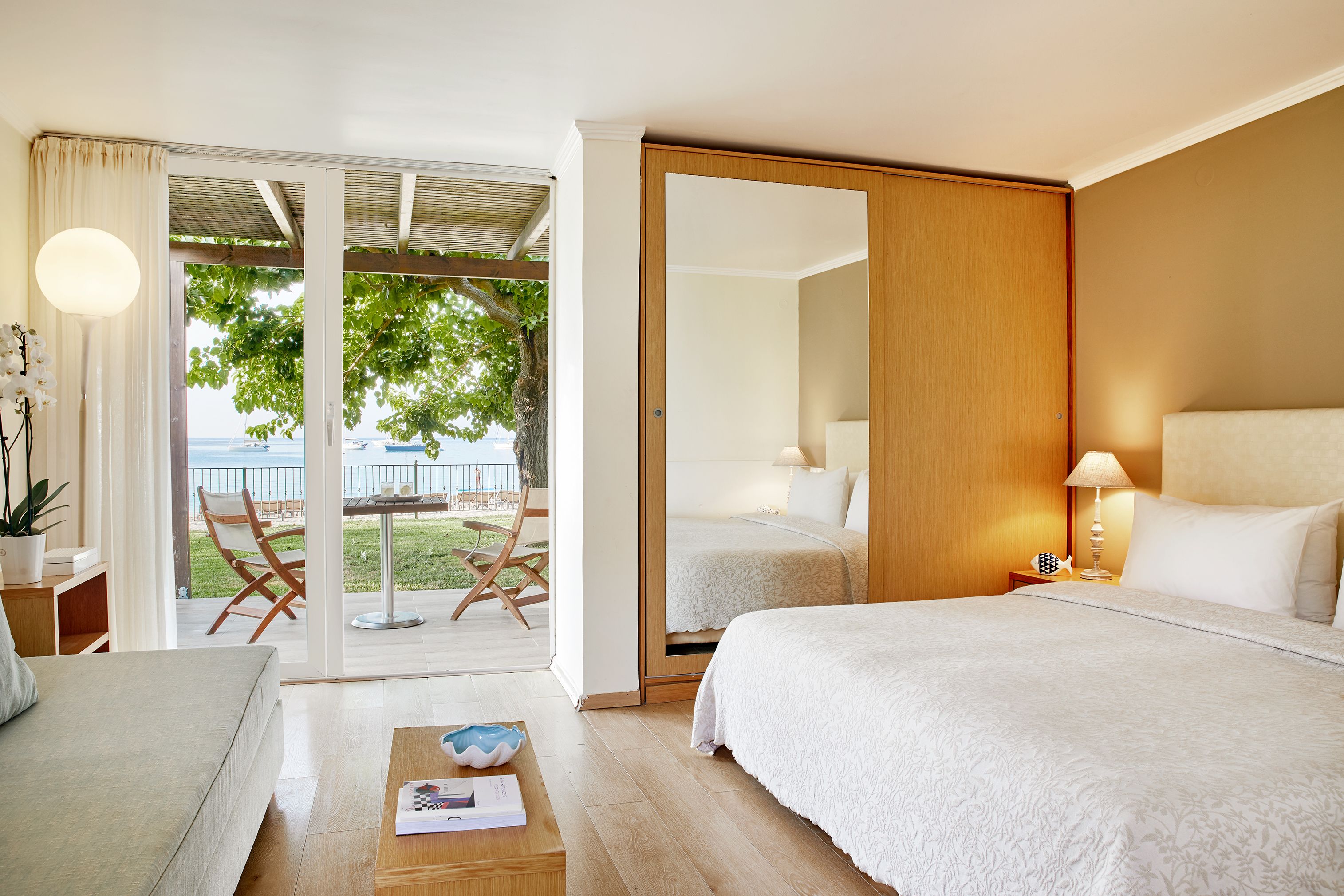 A hotel room with two beds, a sofa, a coffee table, and a view of the sea.