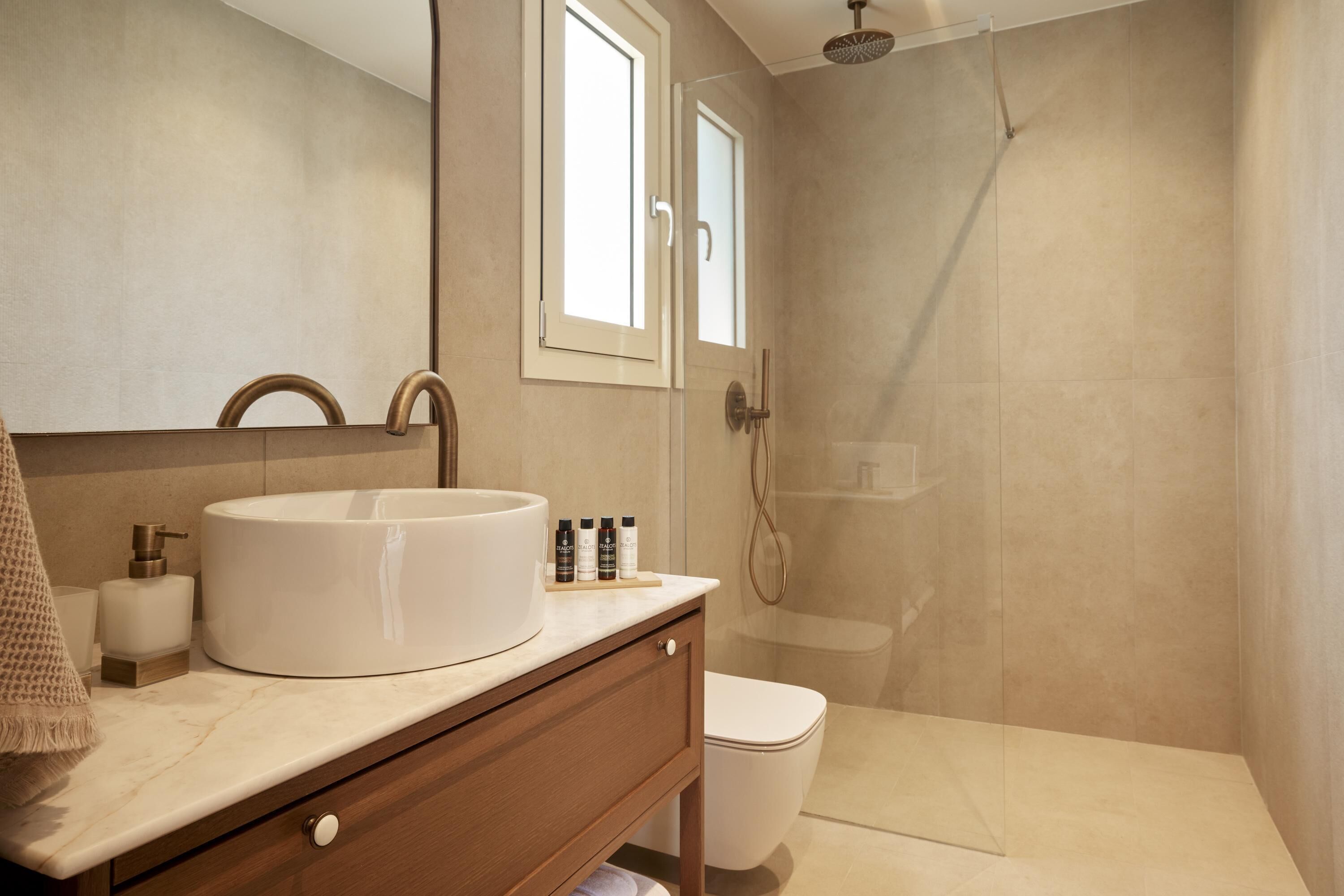 Un baño moderno con un lavamanos blanco grande, un espejo, un mueble de tocador de madera y una zona de ducha.
