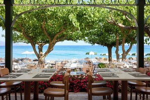 An outdoor dining area with tables and chairs, overlooking a beach and the sea. - Parga Beach Resort (Parga)