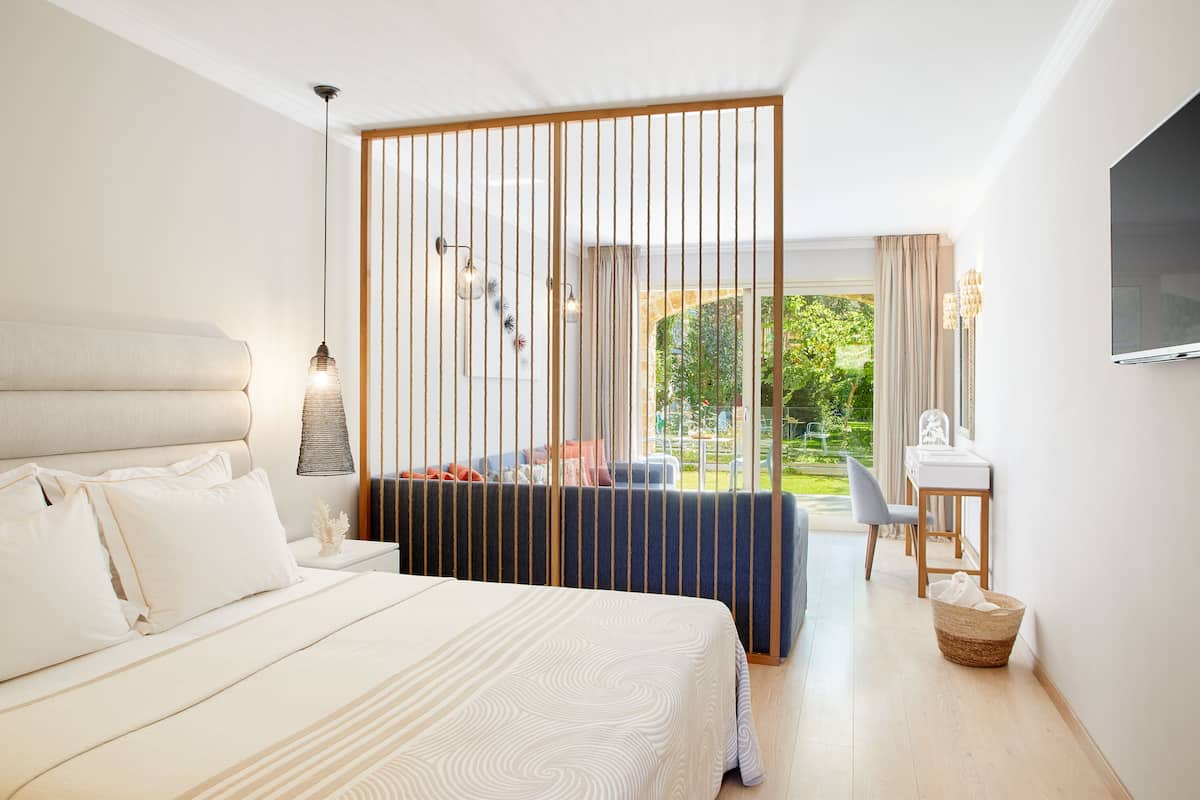 A modern hotel room with a large bed, a desk, and a view of a garden.