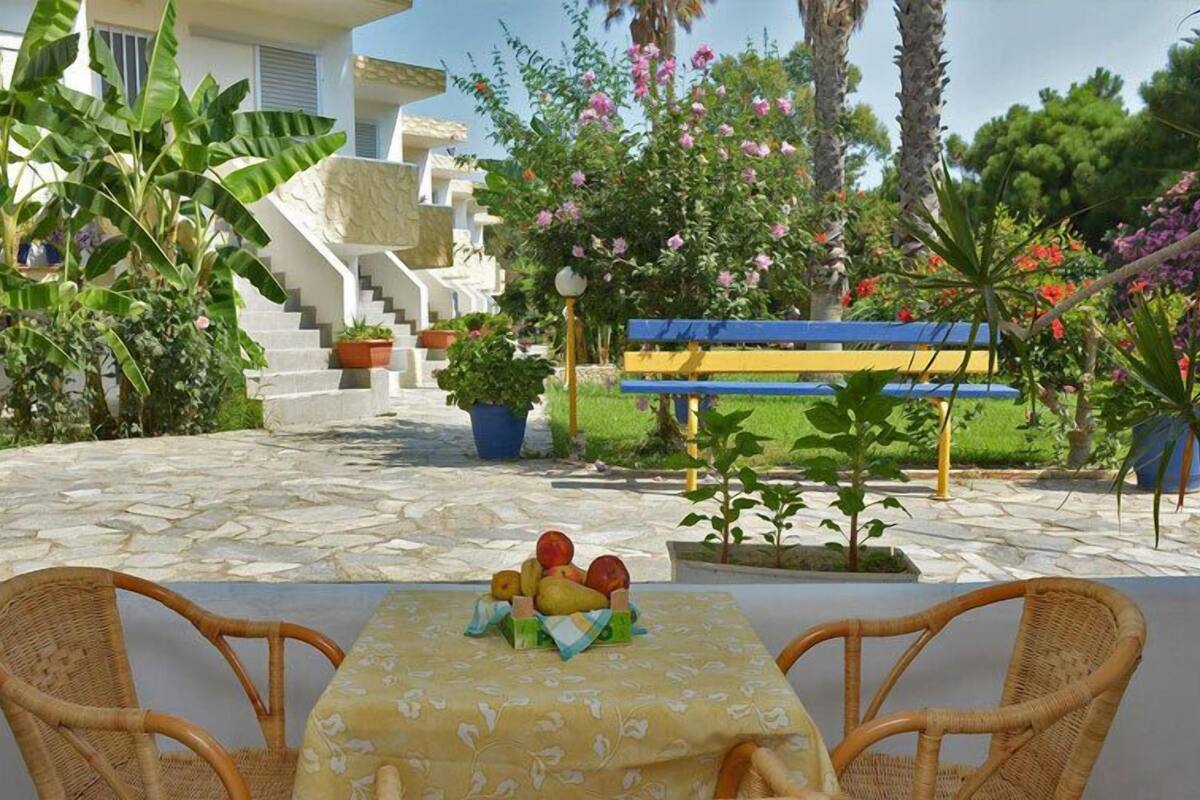 A patio with wicker chairs, a table with fruit, and a bench.