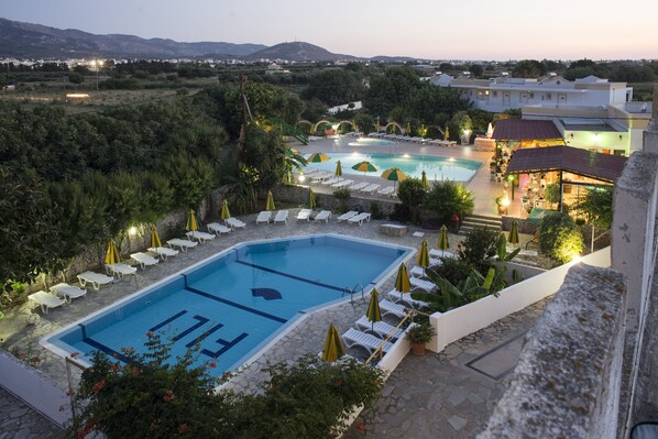 A swimming pool with lounge chairs and umbrellas, surrounded by greenery and buildings.