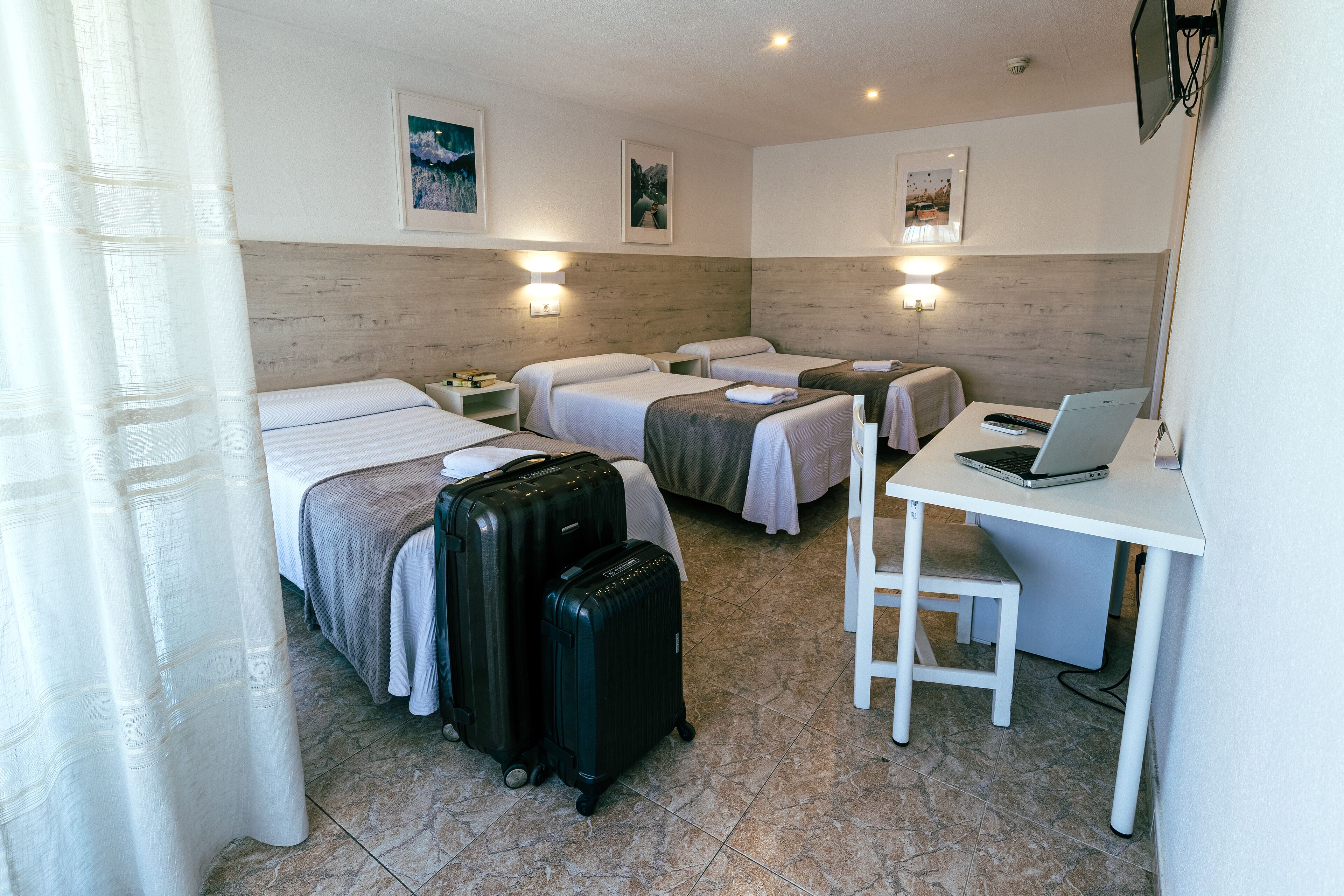 Una habitación de hotel con dos camas, un escritorio con una computadora portátil y dos maletas.