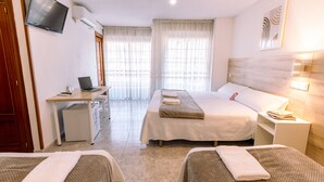 A hotel room with two beds, a desk with a laptop, a TV, and a small seating area. - Hostal Gran Vía (Pinto)