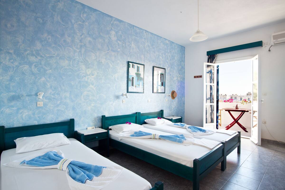 A hotel room with two beds, a balcony with a table and chairs, and a view of the city.