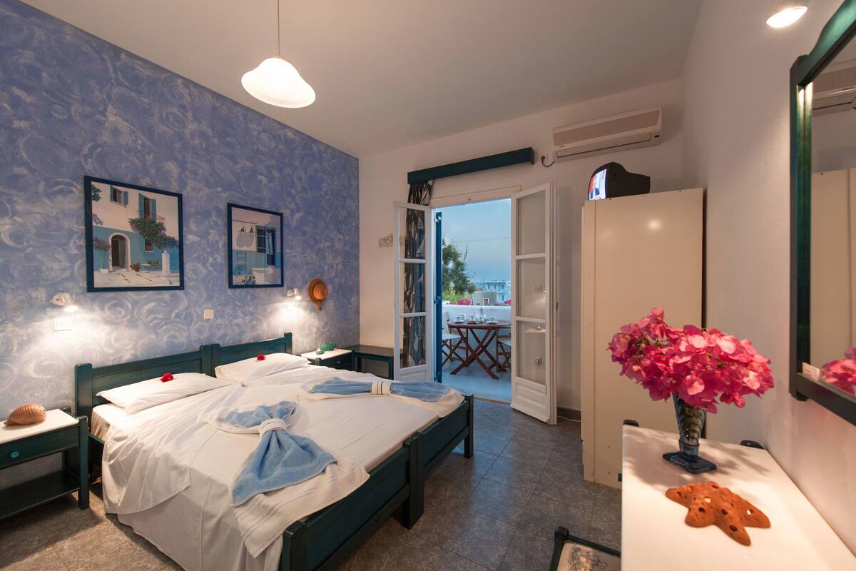A bedroom with two beds, a balcony with a table, and a vase of flowers.