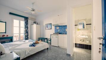 Ein Hotelzimmer mit Bett, Schreibtisch, Deckenventilator, einer Küchenzeile und einem Badezimmer mit Waschbecken und Spiegel.