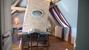 A cozy room with a wooden table and chair, a small mirror on the brick wall, and a window with curtains. - La Cuvellerie (Narcy)