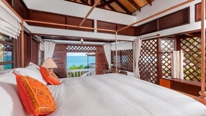 A four-poster bed with white linens and orange pillows, a wooden ceiling, and a view of the ocean through a lattice window. - Baan Khunying – Secluded Phuket Beachfront Villa (Rawai)