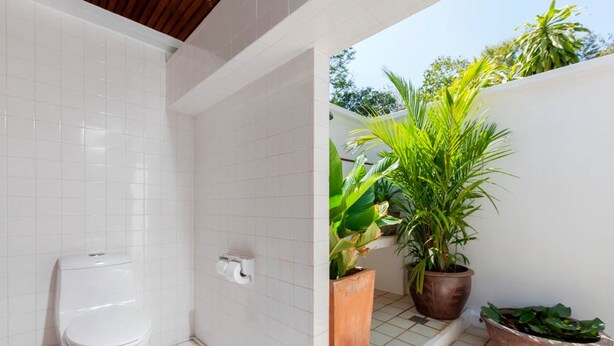 A bathroom with white tiles, a toilet, and a small potted plant. - Baan Khunying – Secluded Phuket Beachfront Villa (Rawai)