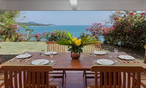 Enjoy a serene dining experience with a scenic view of the sea and distant hills from this outdoor dining area.