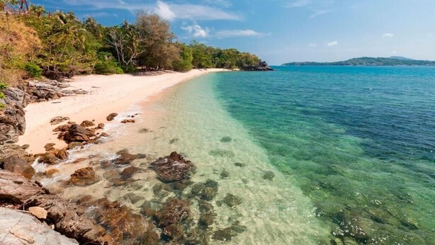 A beach with clear water, rocky shore, and trees. - Baan Khunying – Secluded Phuket Beachfront Villa (Rawai)