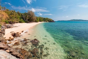 Enjoy a serene beach setting with turquoise waters and a sandy shoreline, bordered by rocky outcrops and lush greenery.