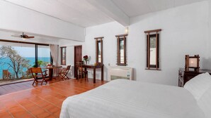 A bedroom with a large bed, a desk with chairs, a view of the sea, and a ceiling fan. - Baan Khunying – Secluded Phuket Beachfront Villa (Rawai)