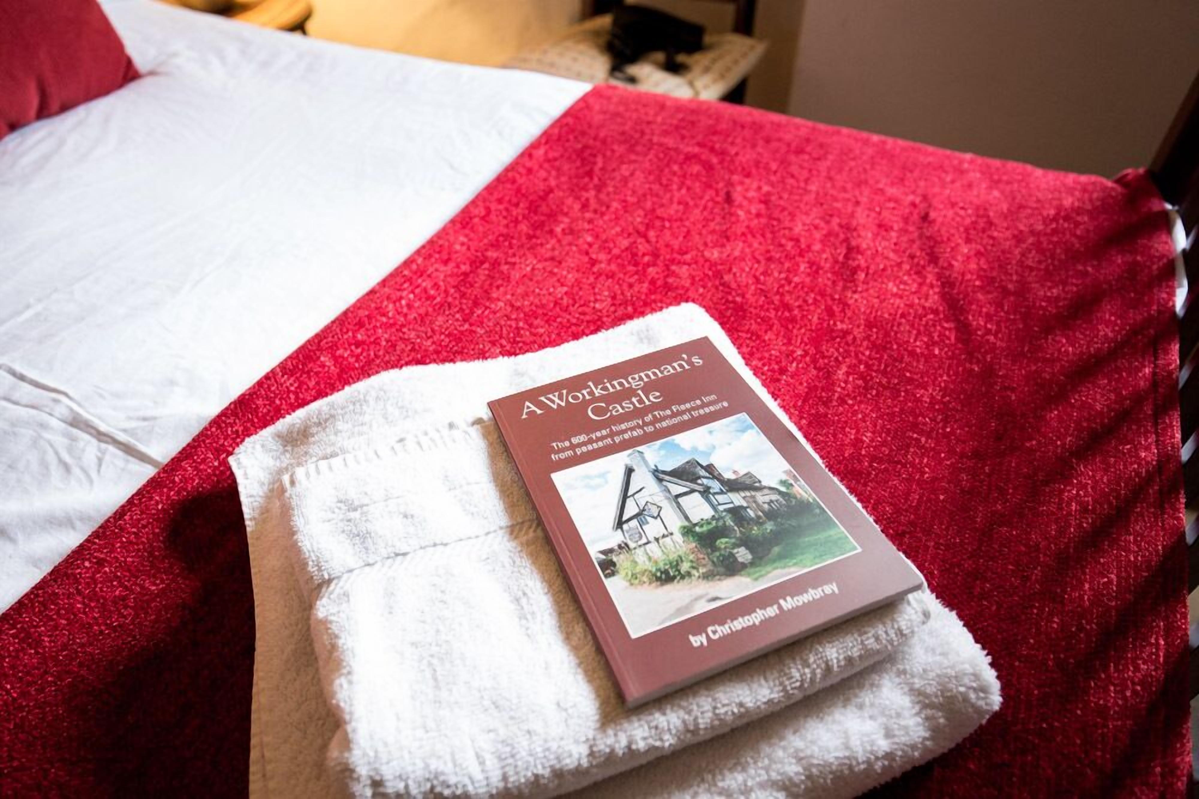 Un libro titulado "A Workingman's Castle" de Christopher Moodyrey sobre una cama con una manta roja y una toalla blanca.