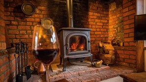 Una habitación acogedora con chimenea de ladrillo, una copa de vino tinto y un televisor montado en la pared.