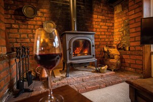 A cozy room with a brick fireplace, a glass of red wine, and a television mounted on the wall.