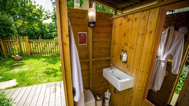 Baño de cabaña de madera con lavamanos, inodoro y una toalla colgada en la puerta.
