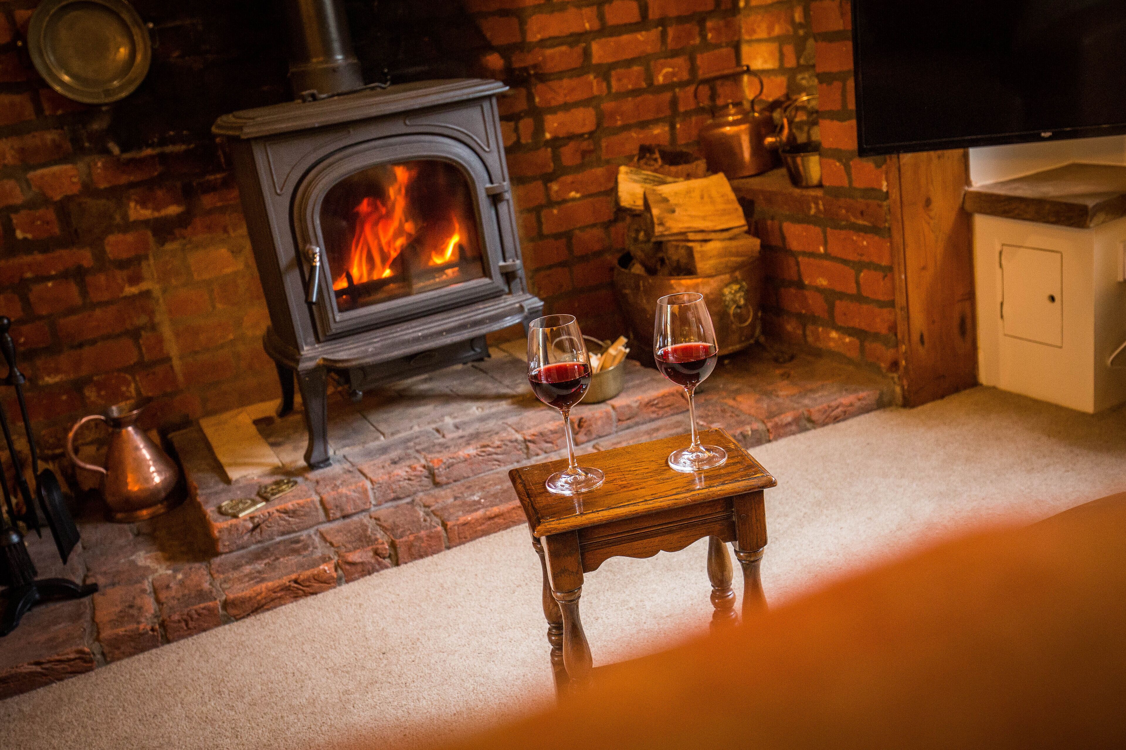 A cozy room with a brick fireplace, a television, and two glasses of red wine on a small wooden table.