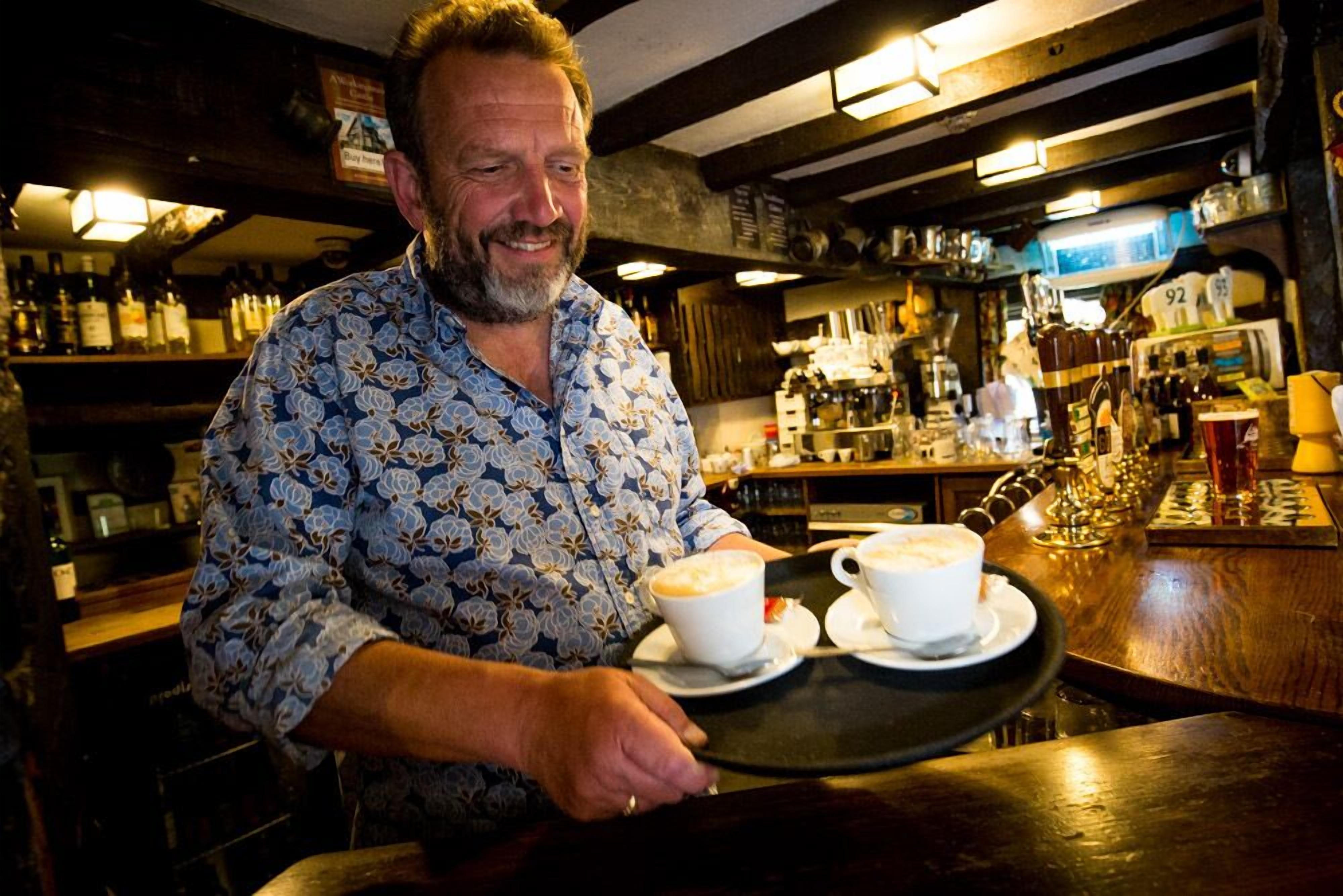 A person serving coffee in a bar setting with shelves of bottles and a counter.