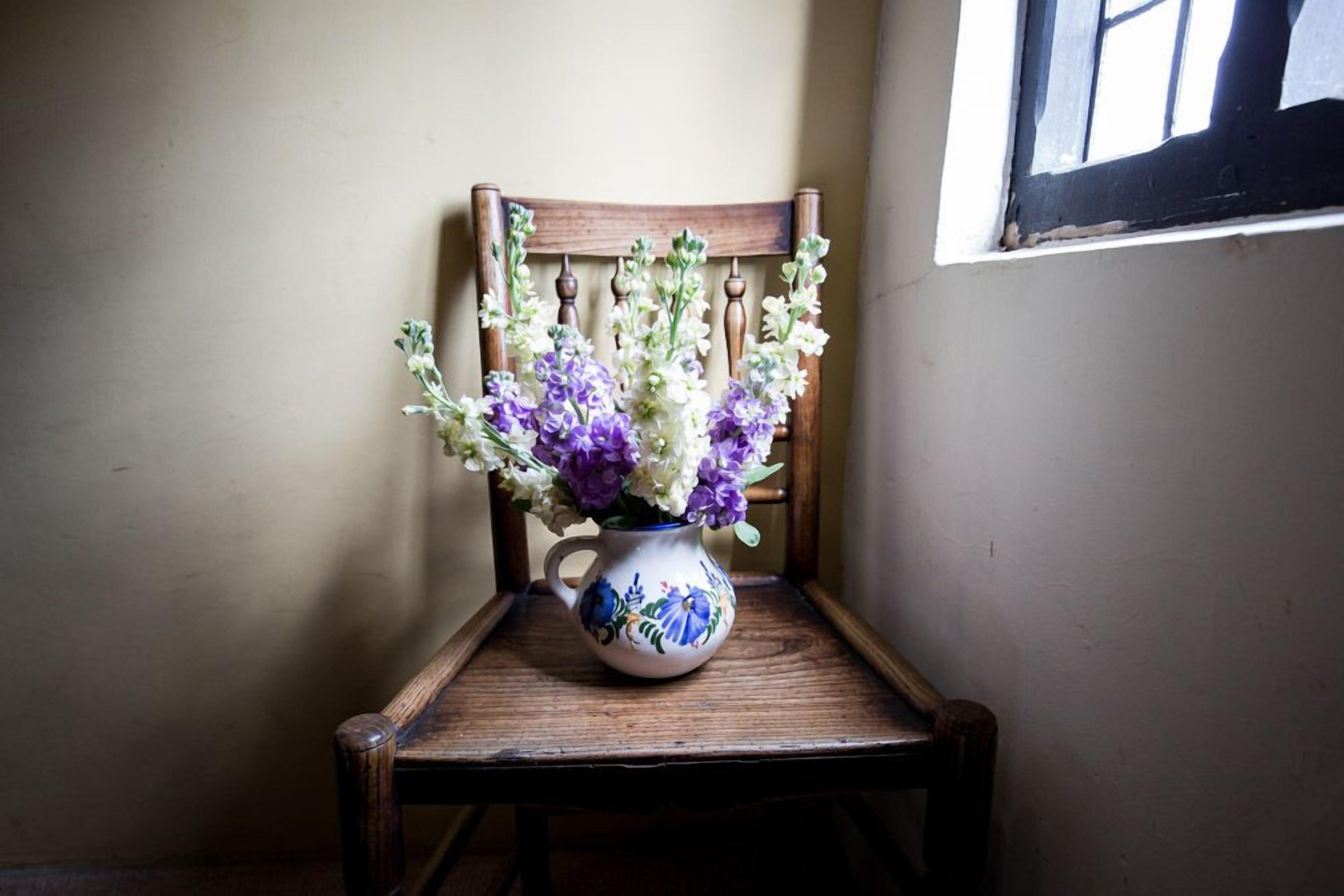 Una silla de madera con un jarrón blanco lleno de flores moradas y blancas.