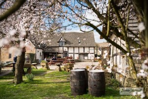 A traditional pub with outdoor seating, stone barrels, and a stone building with a thatched roof.
