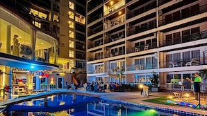 Ein Hotel bei Nacht mit großem Außenpool, mehreren Etagen und einem Restaurant im Erdgeschoss.
