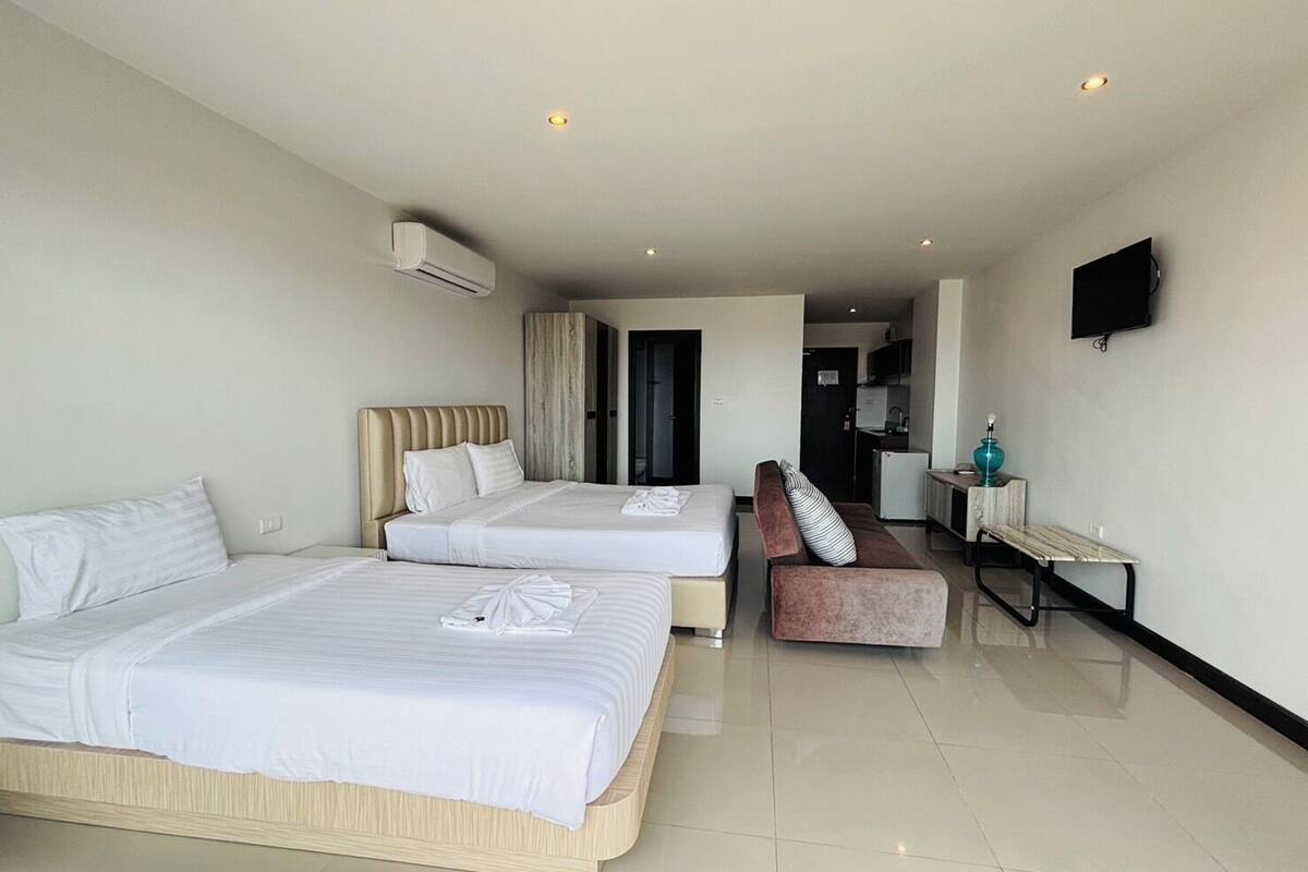 A hotel room with two beds, a sofa, a TV, and a kitchenette.