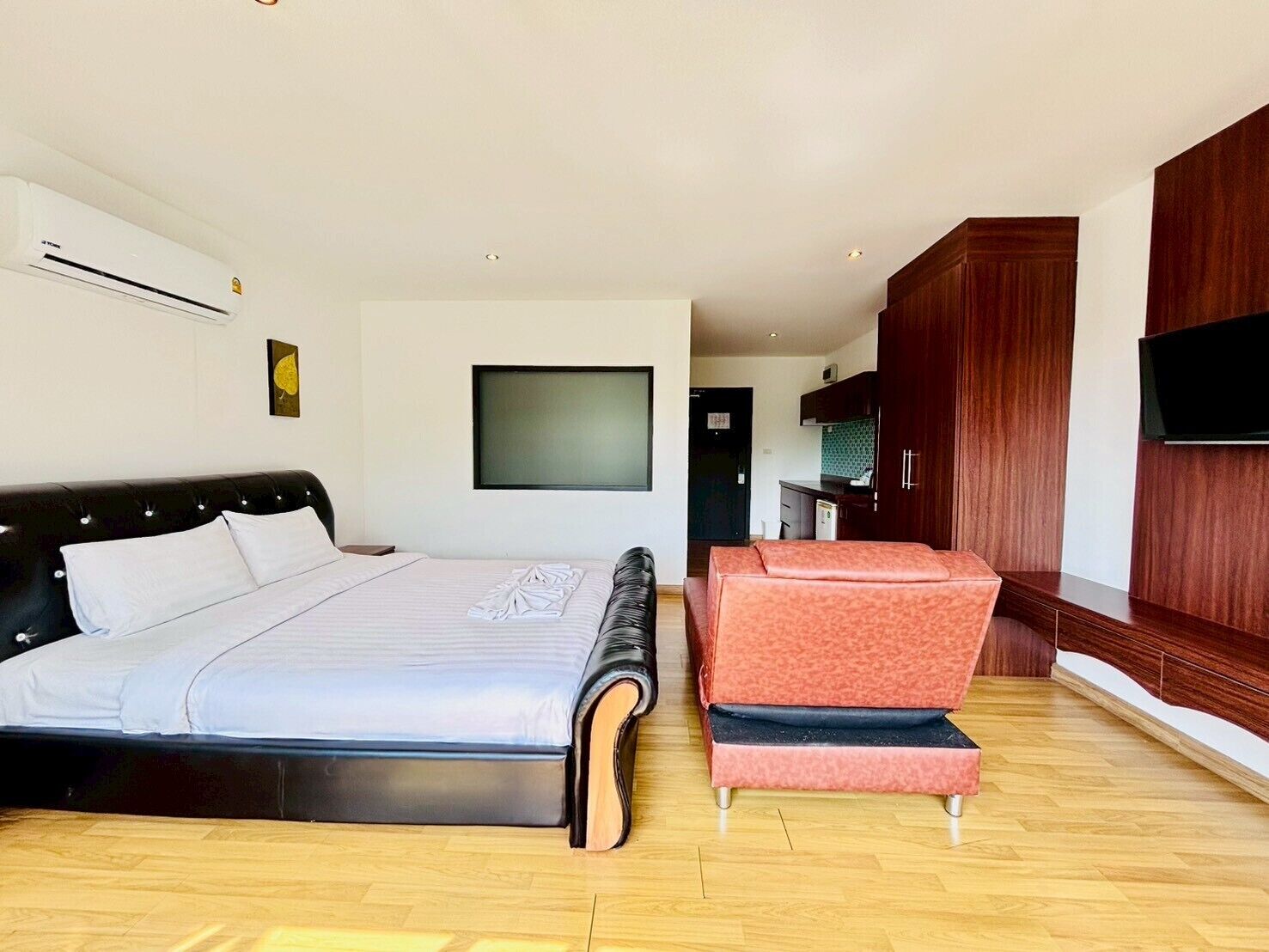 Quarto moderno com cama grande, um cantinho para sentar, televisão e cozinha compacta.