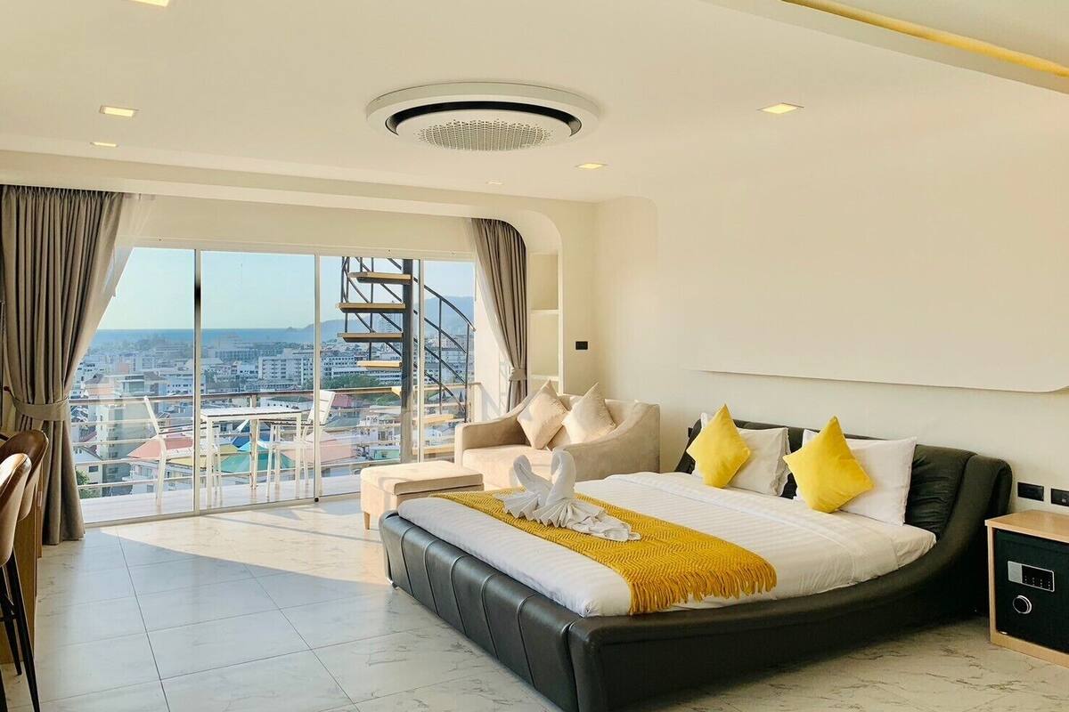 A modern hotel room with a large bed, a view of the city, and a balcony with a spiral staircase.