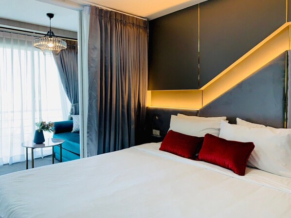 Quarto de hotel moderno com uma cama grande, um espaço de estar com um sofá azul e uma escada.