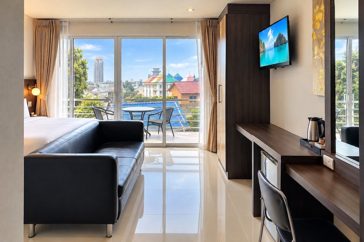 Ein Hotelzimmer mit Bett, Schreibtisch, Stuhl, Fernseher und Blick auf Gebäude und einen blauen Himmel.