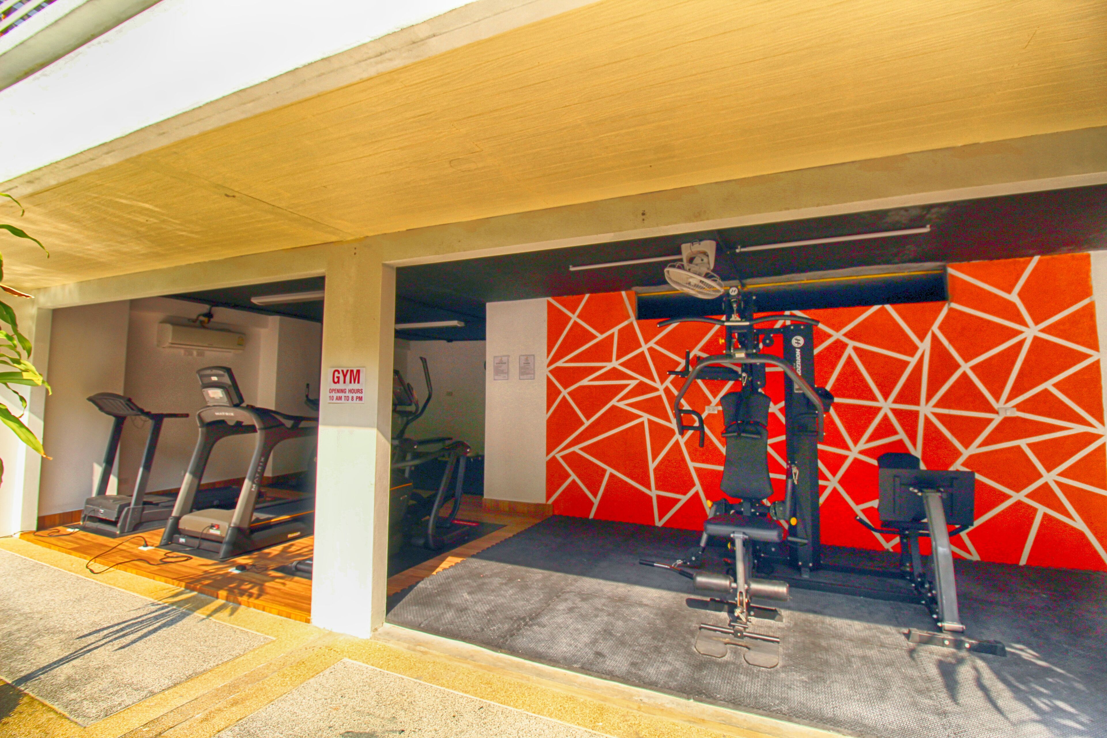 A gym with treadmills and a weight machine, a red geometric wall, and a sign indicating operating hours.